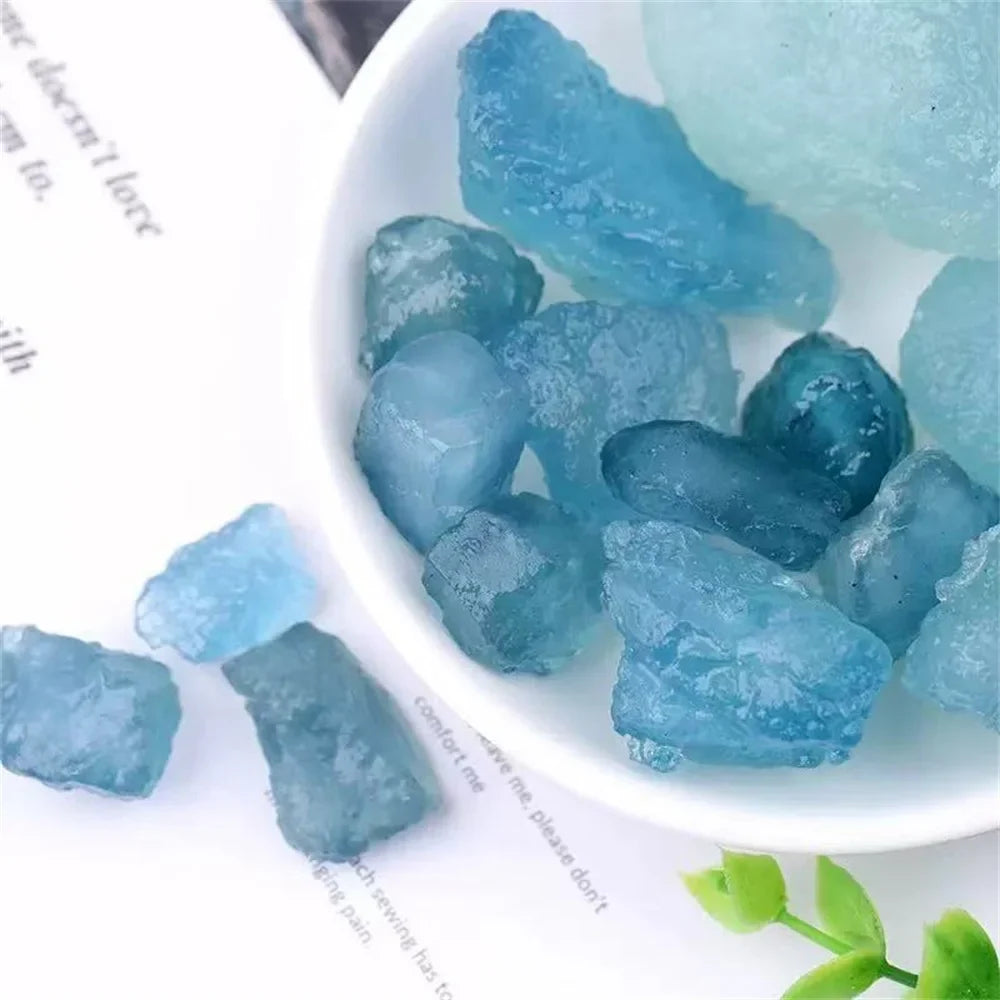 Rough pale blue Aquamarine stones spilling from a white dish in a styled tabletop setting.