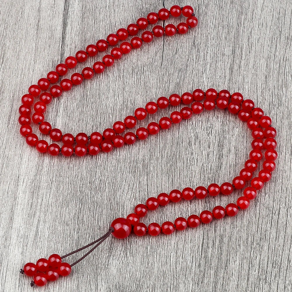 Carnelian mala laid out in a long loop on a gray textured surface.
