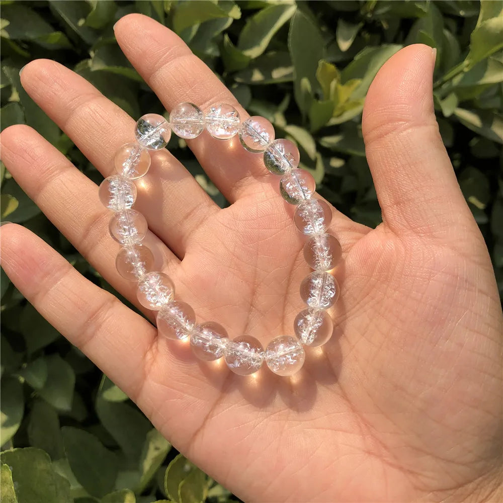 Single Clear Quartz round-bead bracelet held in an open palm outdoors.