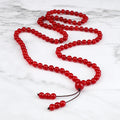 Long red Carnelian mala arranged in a flowing loop on a white marble surface.
