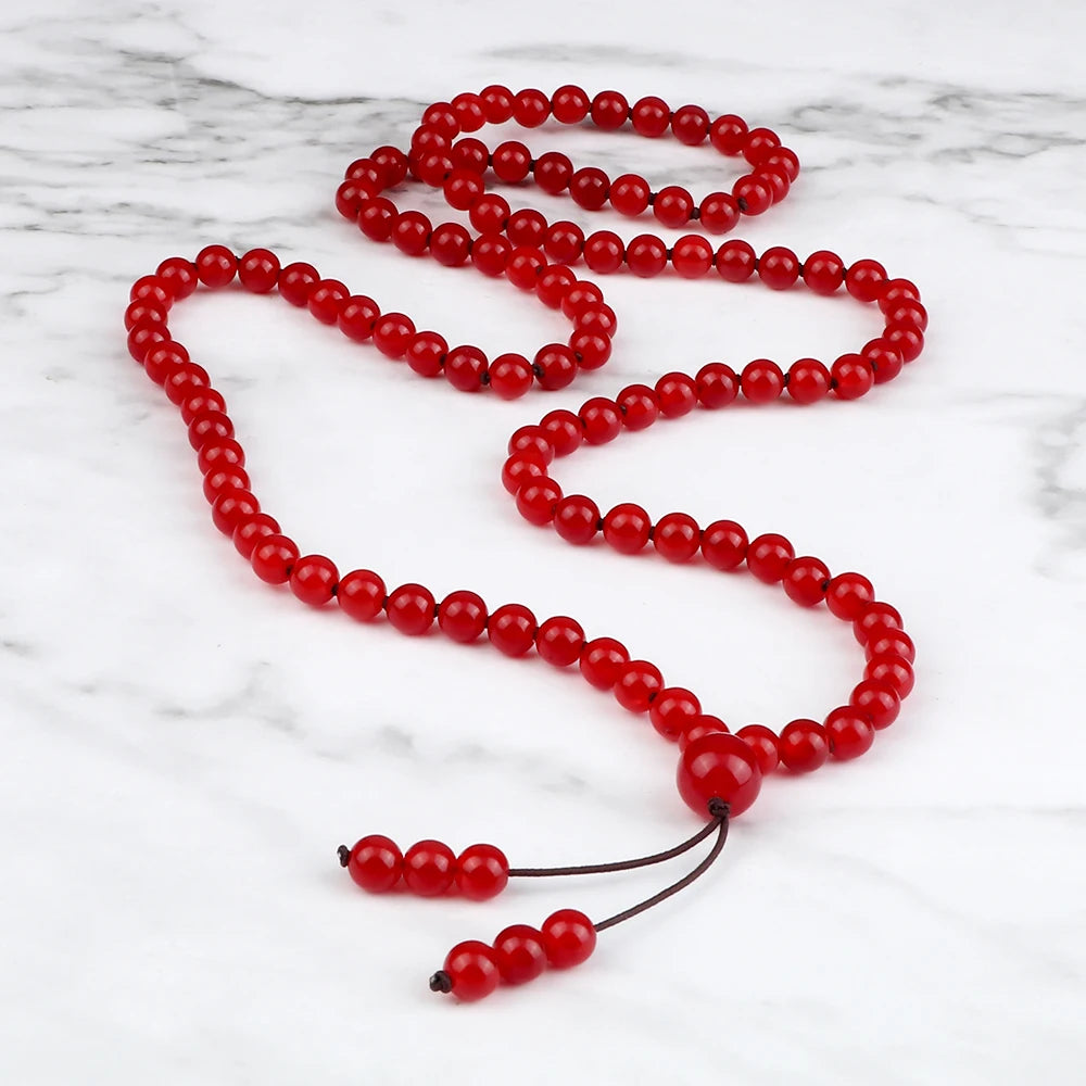 Long red Carnelian mala arranged in a flowing loop on a white marble surface.