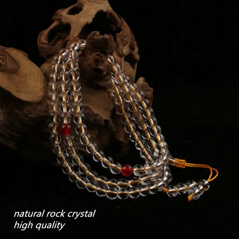 Clear Quartz mala draped over natural wood with red accent beads and yellow cord.