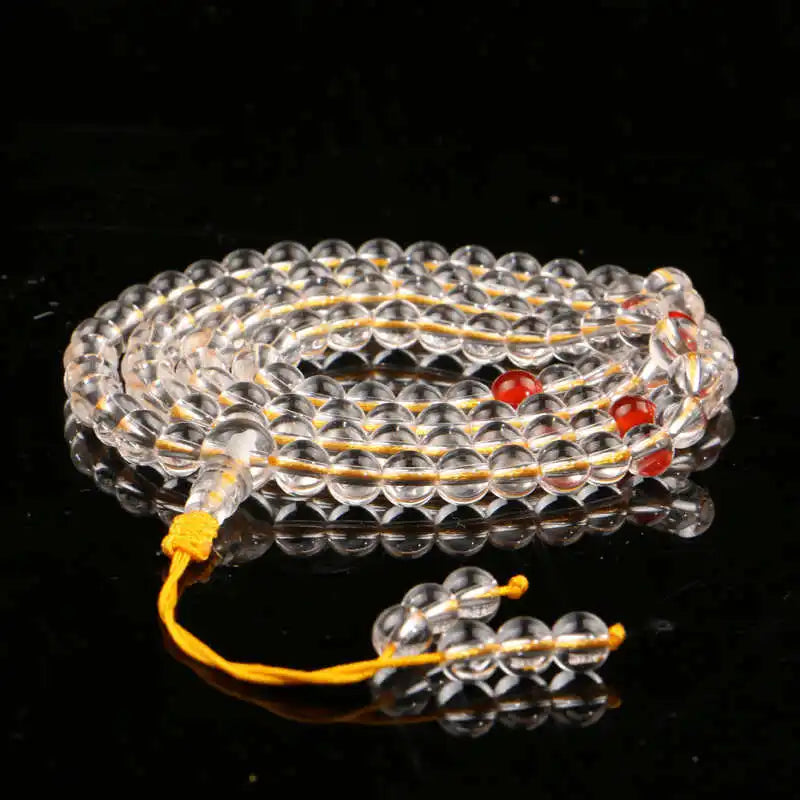 Clear Quartz 108-bead mala coiled on black with red accent beads and yellow cord.