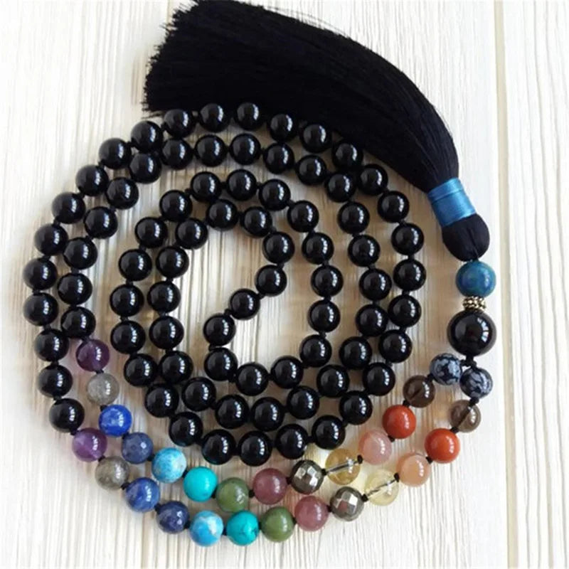 Black Tourmaline tassel mala arranged in loops with multicolor accent beads on a light wood background.