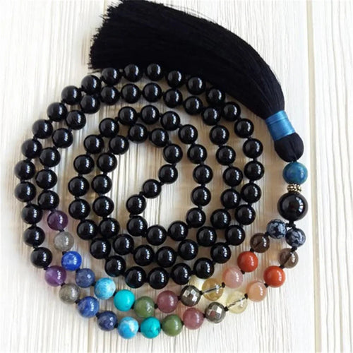 Black Tourmaline tassel mala arranged in loops with multicolor accent beads on a light wood background.