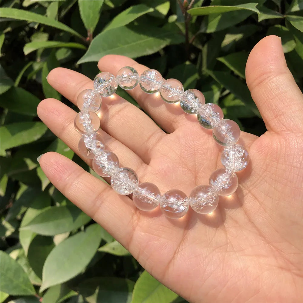 Clear Quartz bead bracelet held in a palm against green foliage.