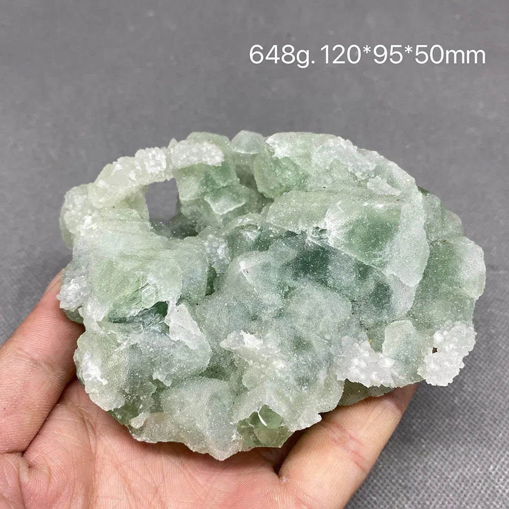 Hand holding a pale green cubic Fluorite cluster with white crystal coating.