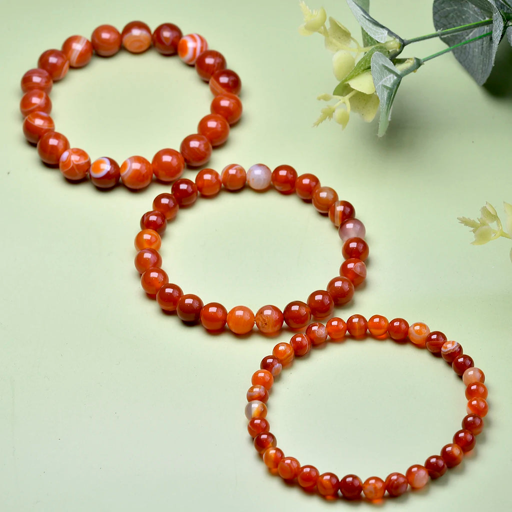 Three Carnelian bead bracelets displayed together in a light botanical setting.
