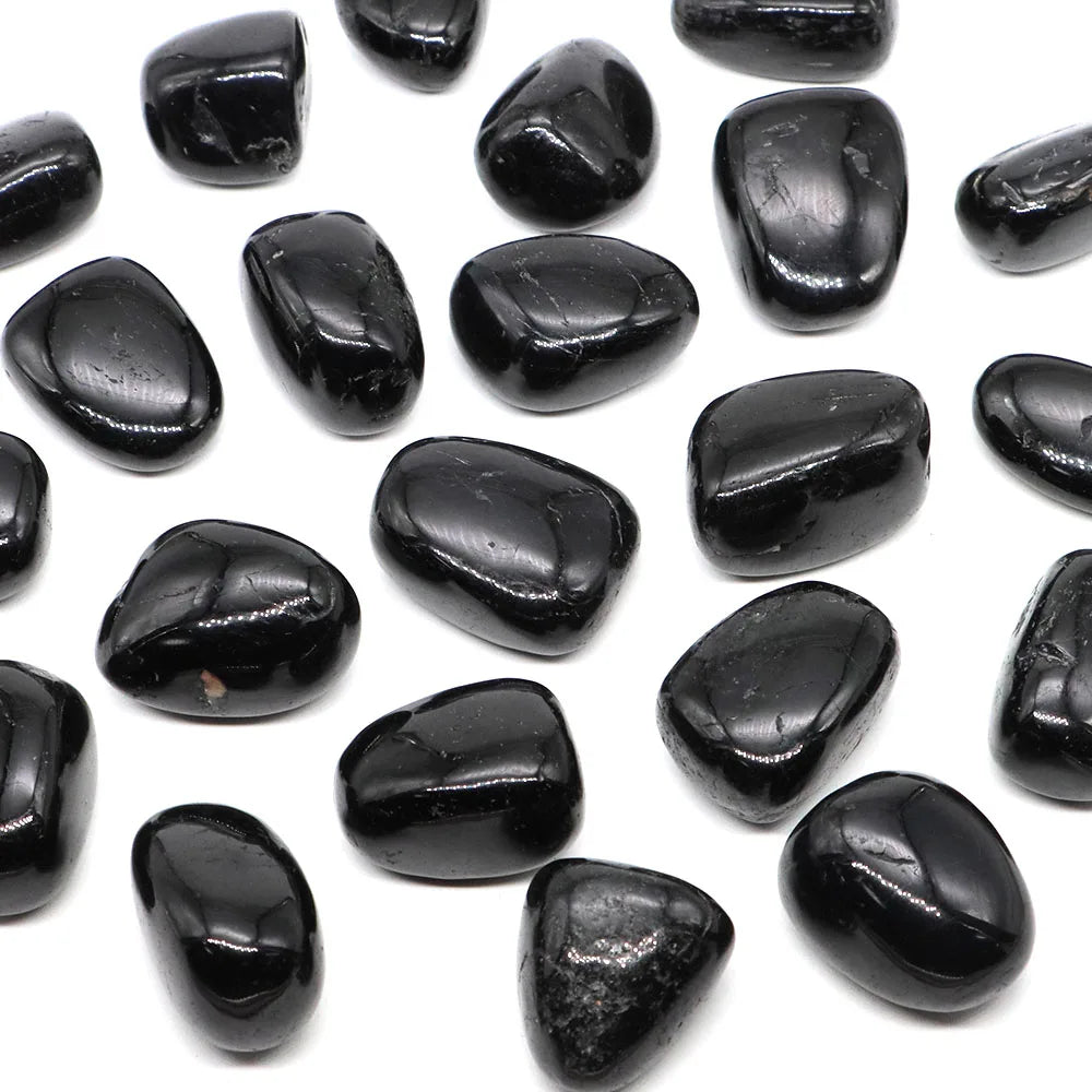 Assorted glossy black Black Tourmaline tumbled stones scattered on a white background.