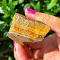 Close-up of a hand-held rough Tiger’s Eye piece showing golden-brown banding.