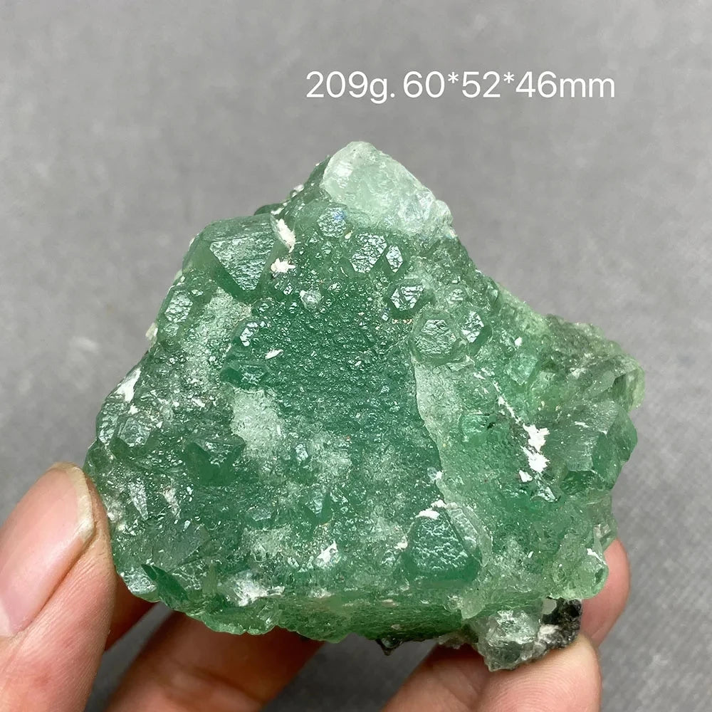Hand holding a vivid green rough Fluorite chunk with translucent areas.