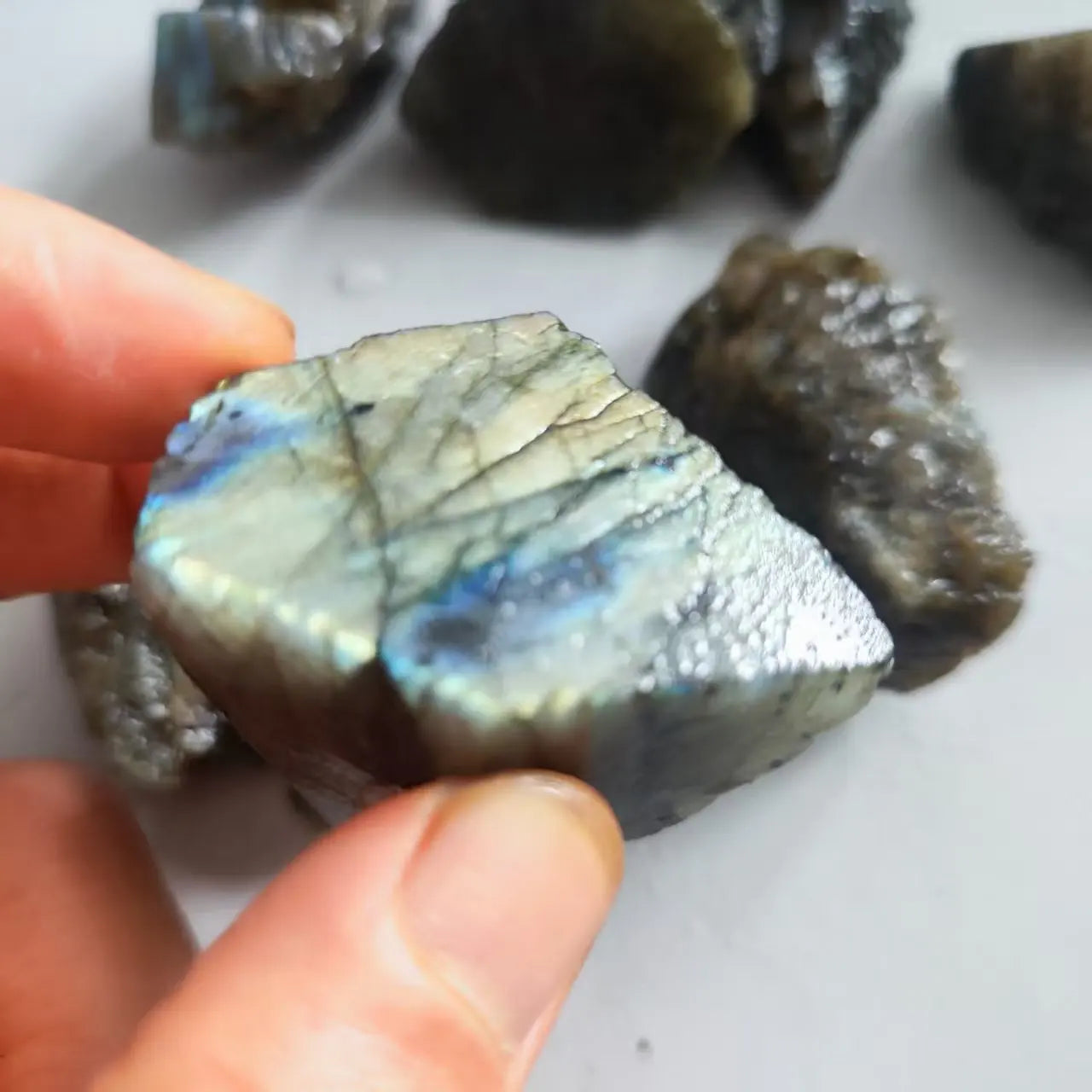 Close-up of a hand-held Labradorite piece with a strong blue-green iridescent face.