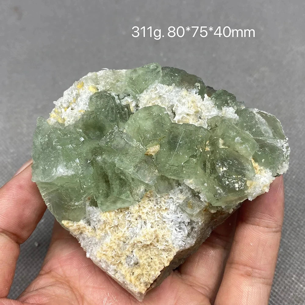 Hand holding a pale green Fluorite cluster with cubic crystal faces.