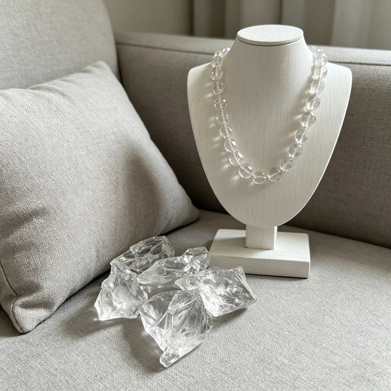 Raw Clear Quartz pieces arranged below a crystal necklace on a white jewelry bust.