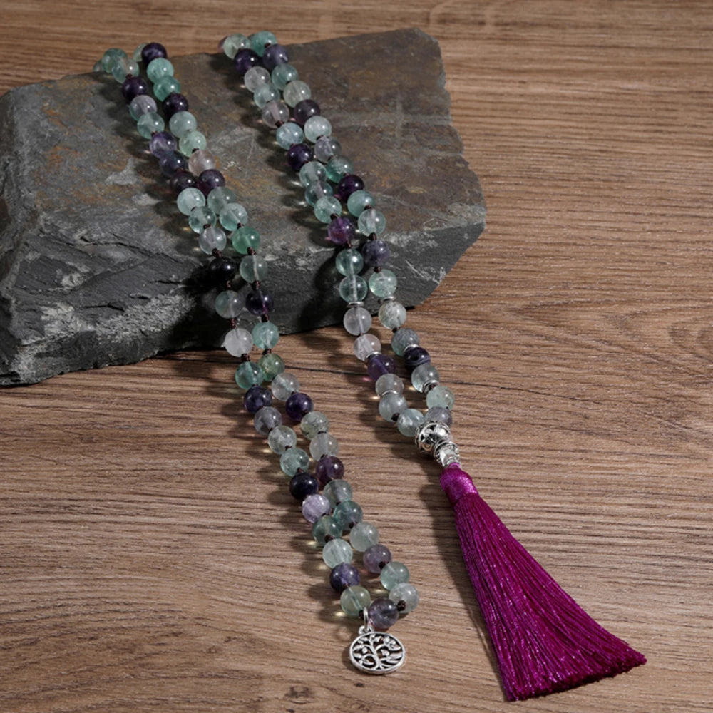 Green and purple Fluorite tassel mala arranged on a wood surface with a silver tree charm.