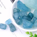 Rough pale blue Aquamarine stones spilling from a white dish in a styled tabletop setting.