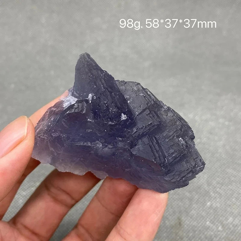 Hand holding a deep purple rough Fluorite specimen.