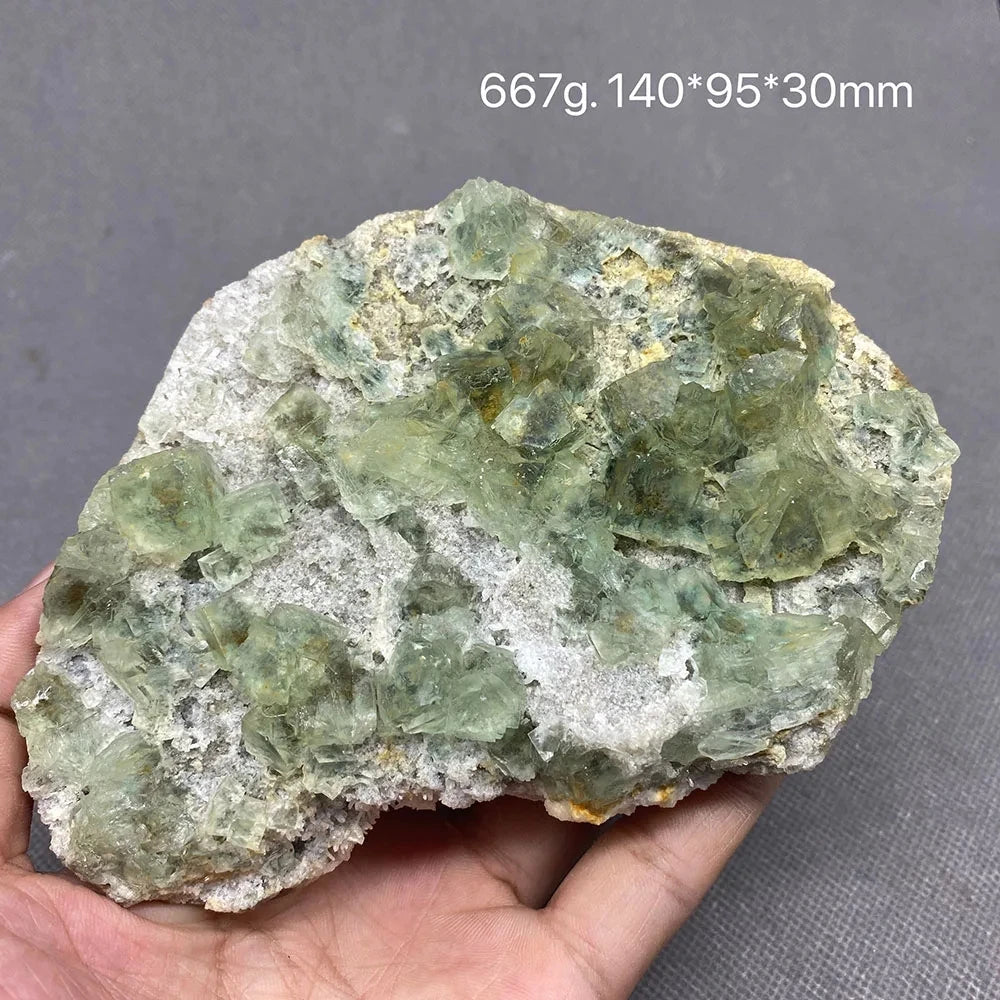 Hand holding a mottled green Fluorite specimen on natural matrix.
