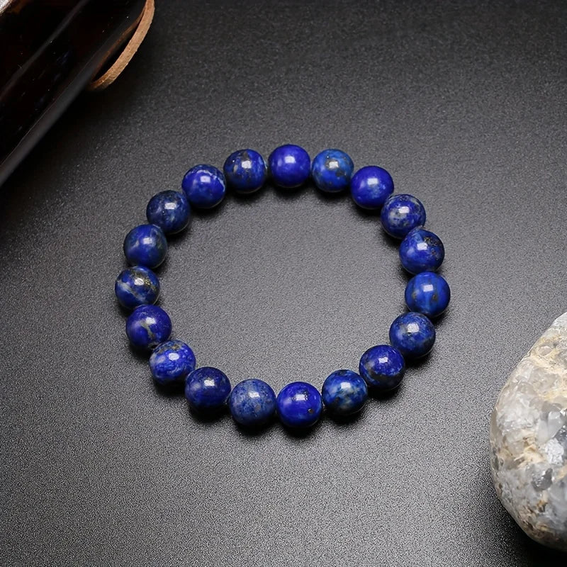 Deep blue Lapis Lazuli round-bead bracelet displayed on a dark surface beside a pale stone.