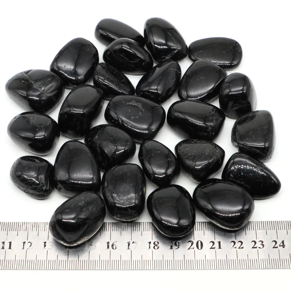 Black Tourmaline tumbled stones arranged above a ruler for scale.