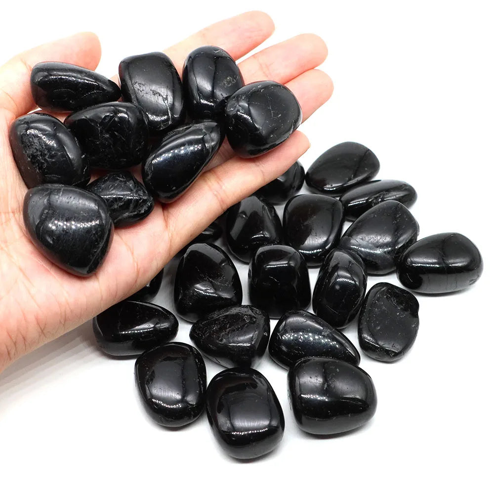 Hand holding smooth polished Black Tourmaline tumbled stones with additional stones below.
