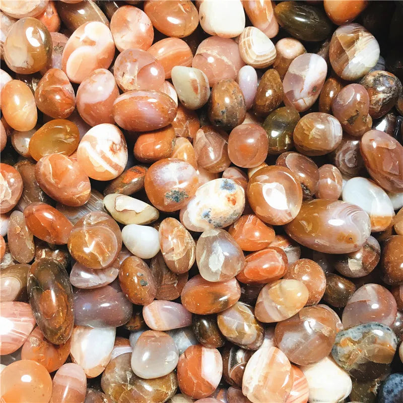 Pile of polished Carnelian stones showing varied orange, cream, and brown patterns.