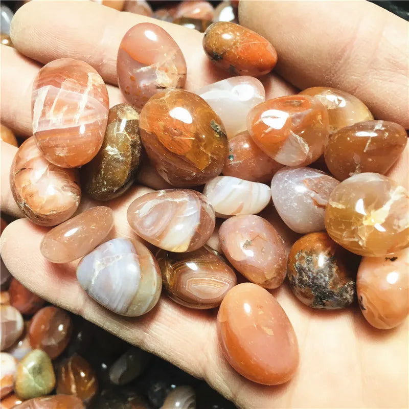Hand holding assorted polished Carnelian stones in orange, brown, and banded tones.