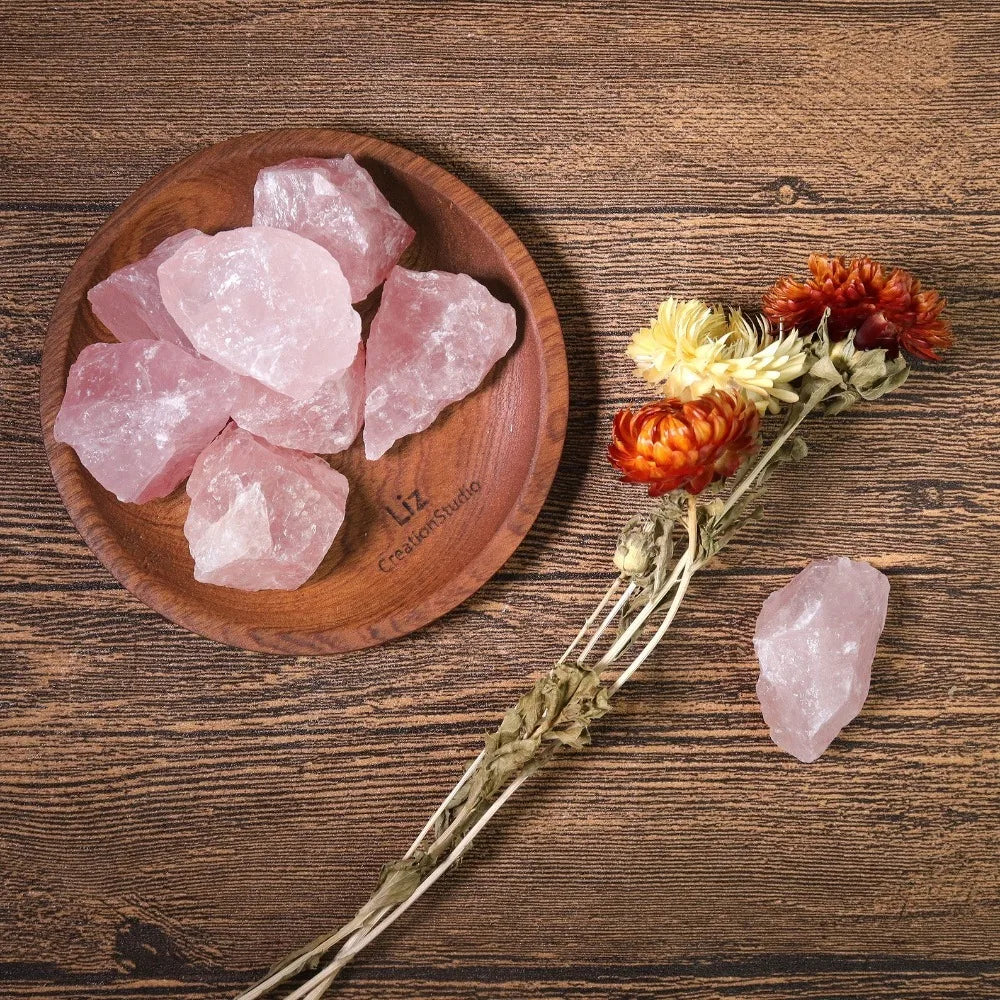 Several rough Rose Quartz pieces arranged on a small wood dish with dried flowers.