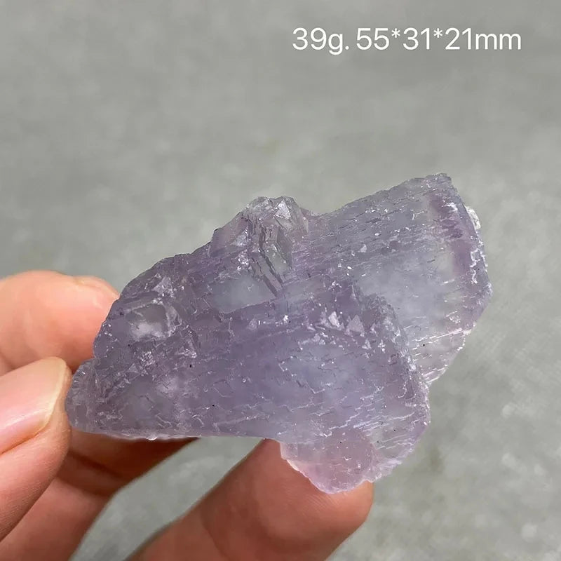 Hand holding a translucent purple rough Fluorite piece.