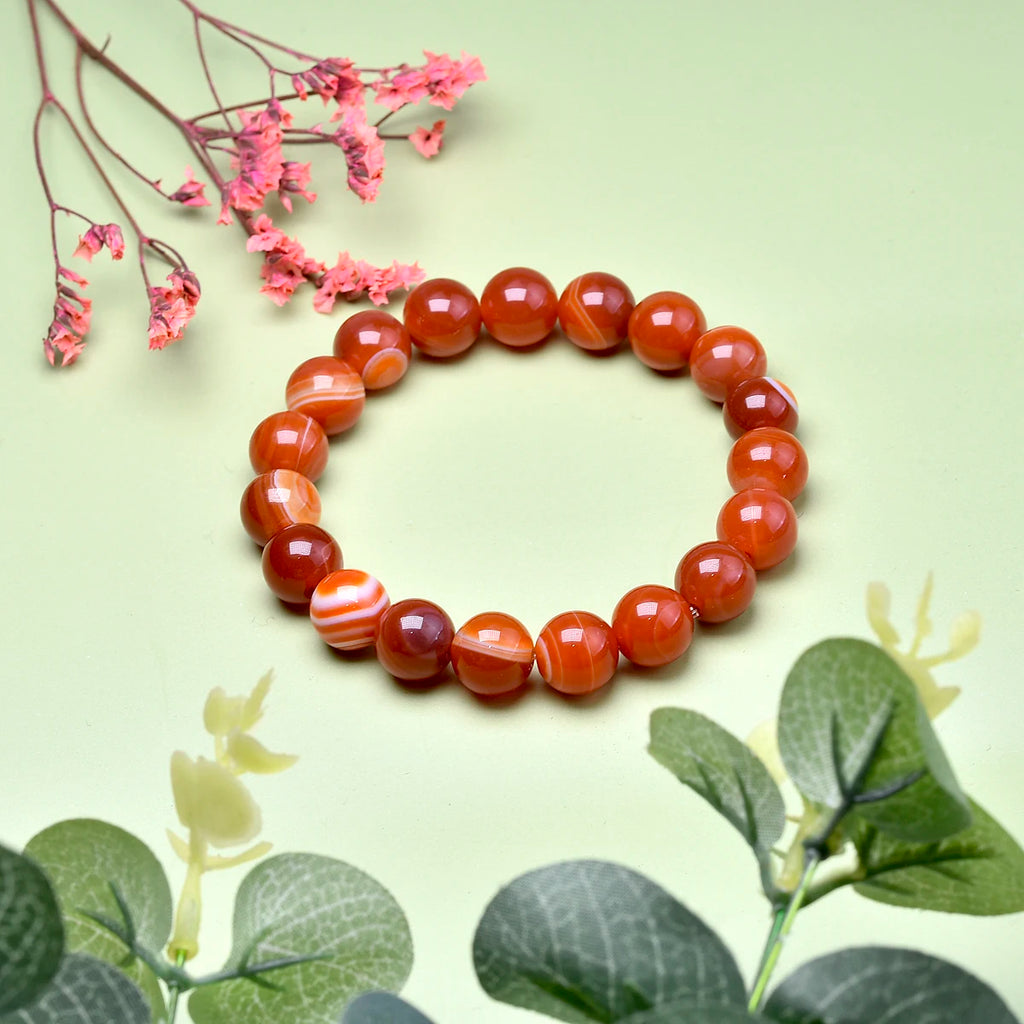 Carnelian bead bracelet styled with pink flowers and green leaves.