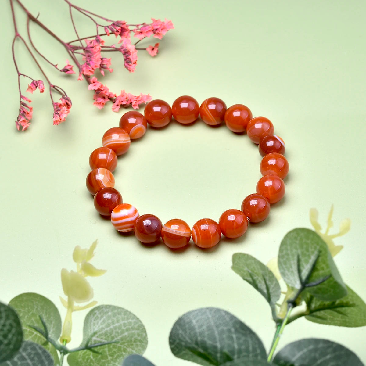 Carnelian bead bracelet styled with pink flowers and green leaves.