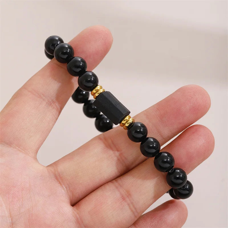 Hand holding a black bead bracelet with a rectangular Black Tourmaline center stone and gold-tone spacers.