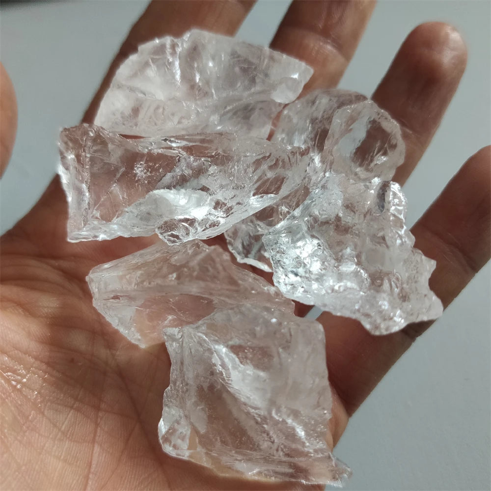 Hand holding several rough transparent Clear Quartz chunks in natural light.